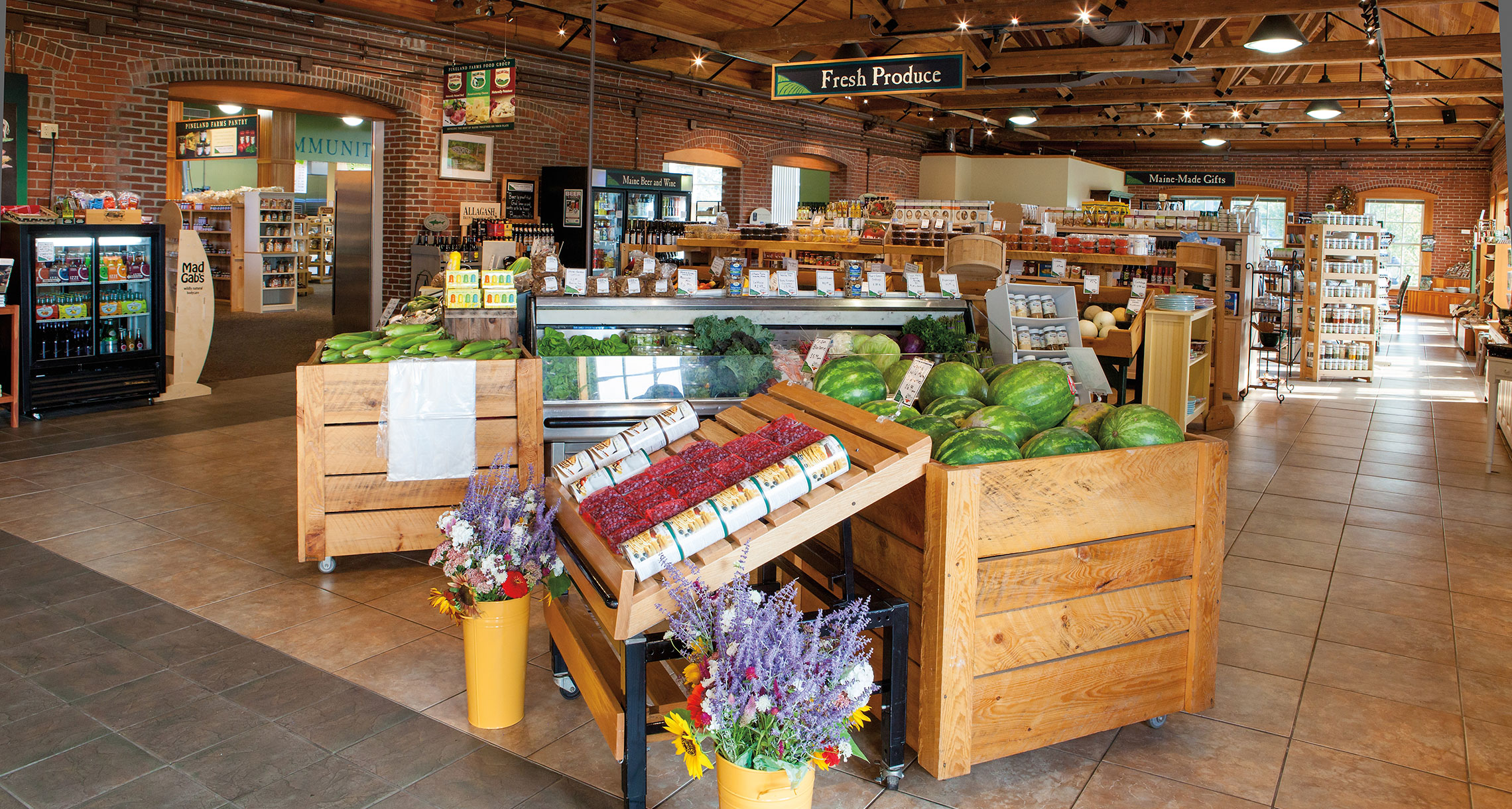 Colorful grocery market with sandwiches, and vegetables and produce in wooden stands.